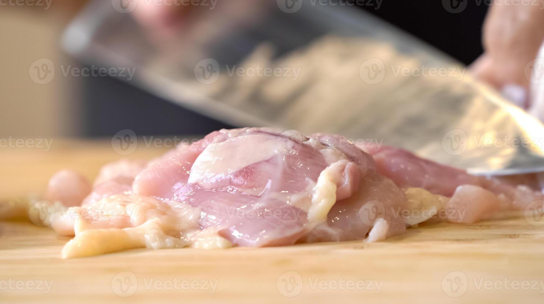 A chef using a kitchen knife slices uncooked chicken meat on a chopping board, the close up view of preparing food ingredients. photo