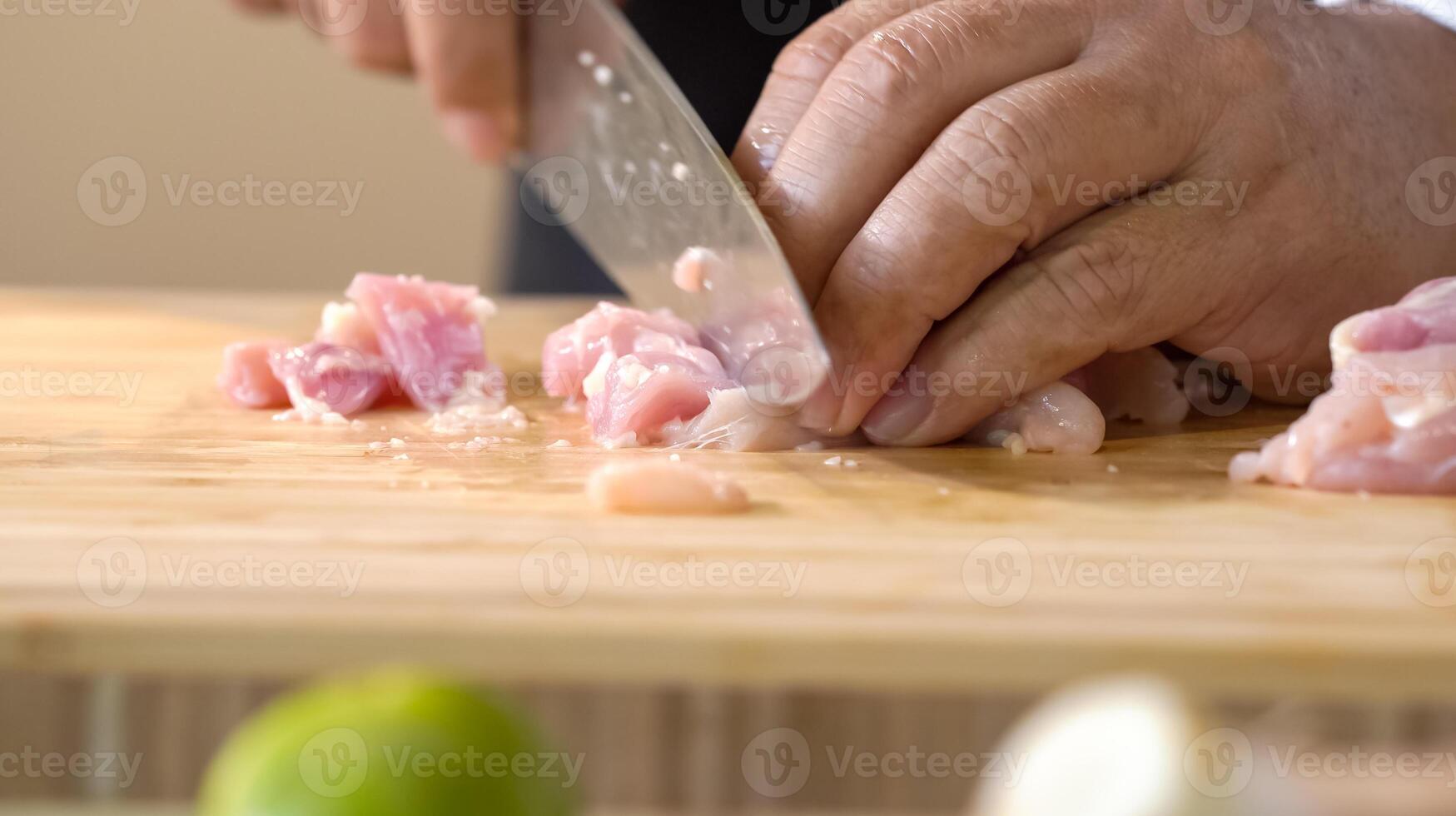 A chef using a kitchen knife slices uncooked chicken meat on a chopping board, the close up view of preparing food ingredients. photo