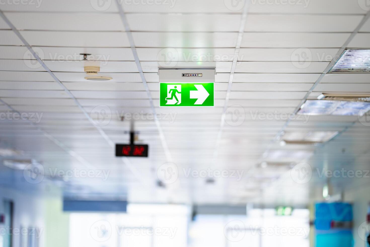 Green White light neon sign depicting a fire exit with interior mirror door background. It's hung on ceiling. photo