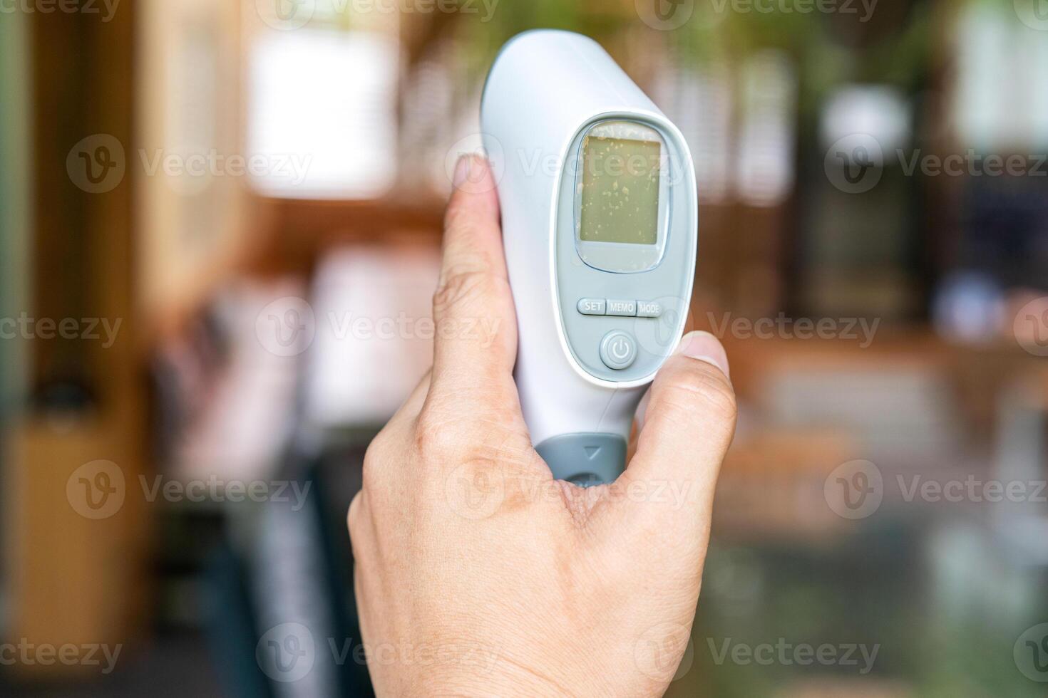 Thermometer Gun in Man's Hand. It is Digital Infrared Sight Temperature Measurement Device on wood table in outdoor field. Clipping Path. photo