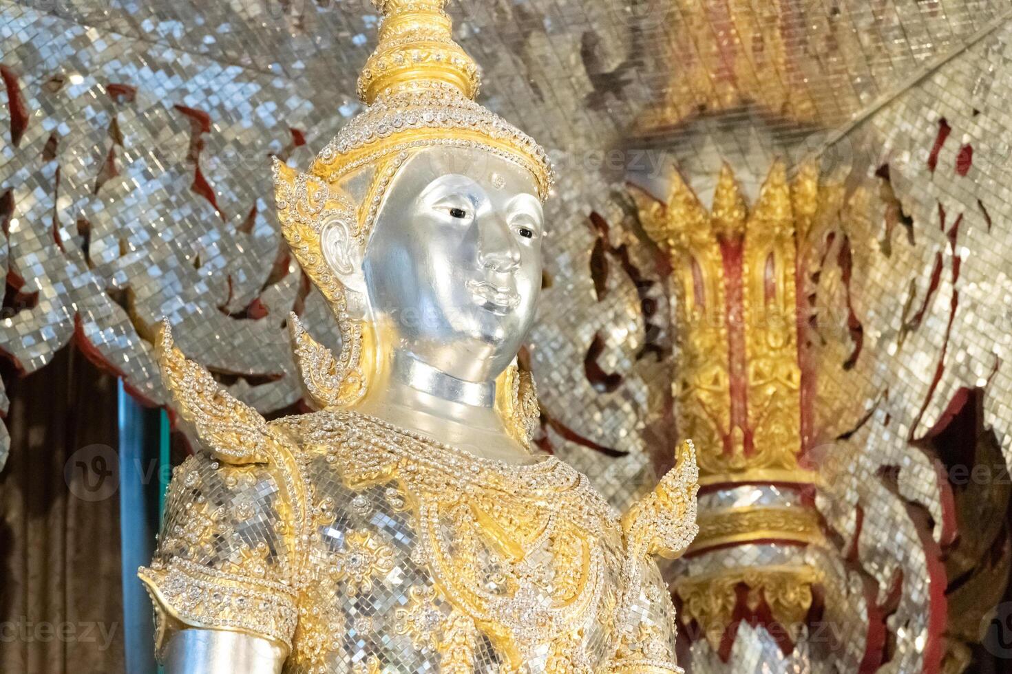 Deity statue standing straight made of silver, wearing silver gold costume with Chada on top of his head. Surrounded by sparkleling decoration. photo
