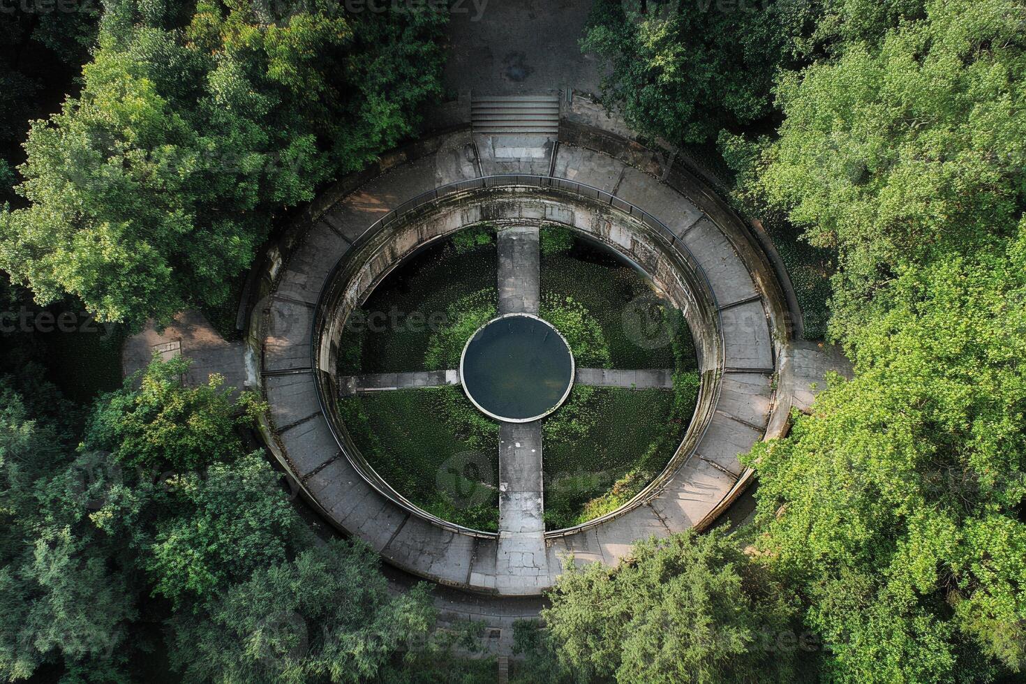 Aerial view of a circular stone structure with a central pond, surrounded by lush green trees. photo