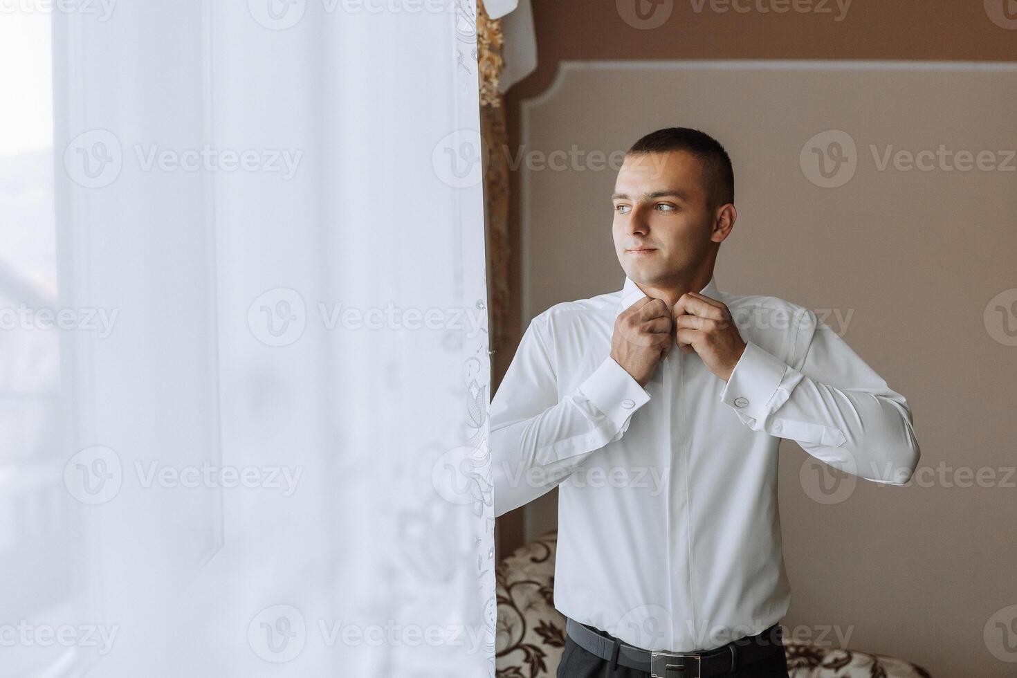 A man in a white shirt is getting dressed in front of a window photo