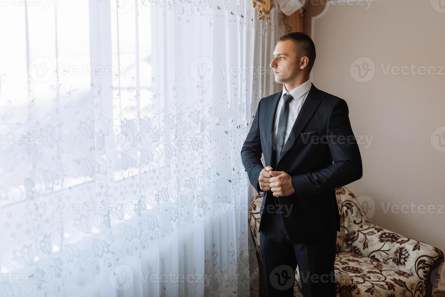A man in a suit is standing in front of a window, looking out at the street photo