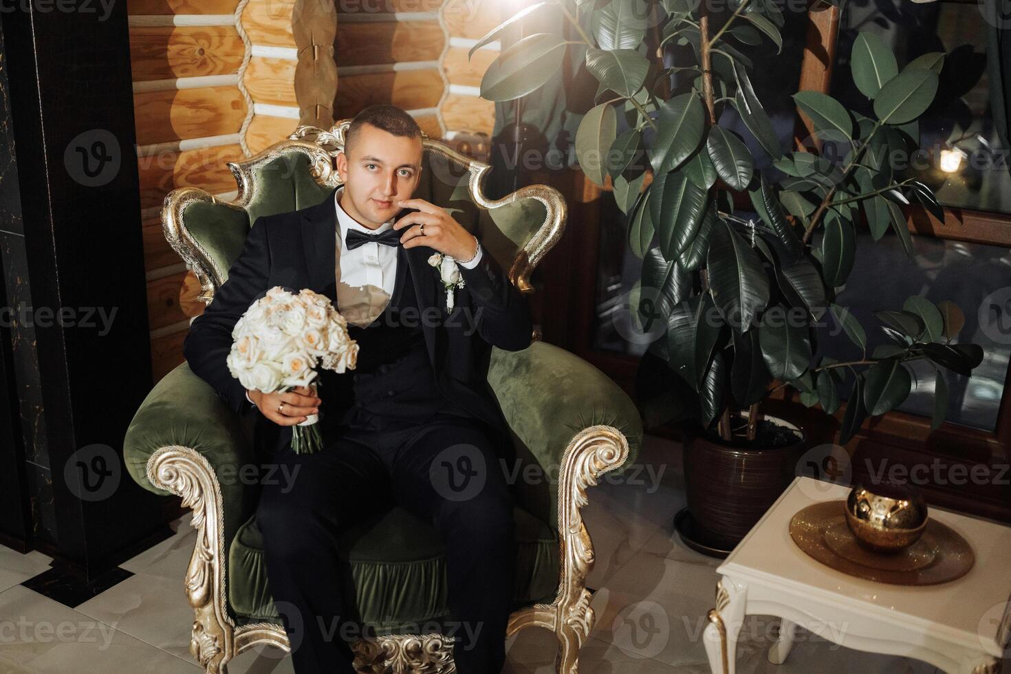 A man in a suit is sitting in a green chair with a bouquet of flowers in his lap photo