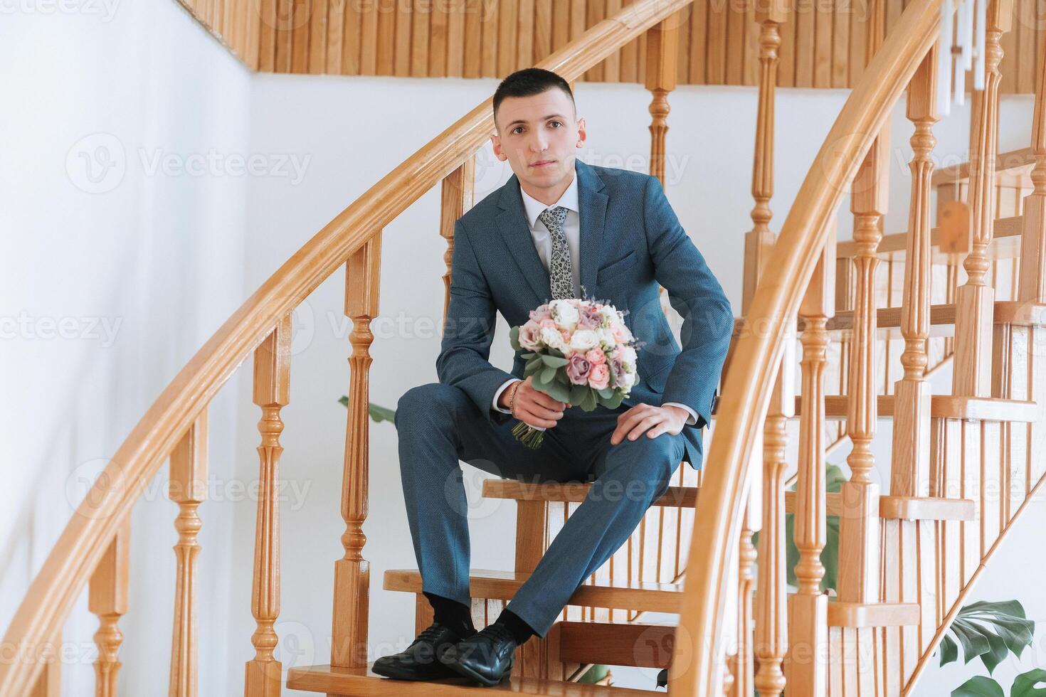 A man in a suit is sitting on a staircase holding a bouquet of flowers photo