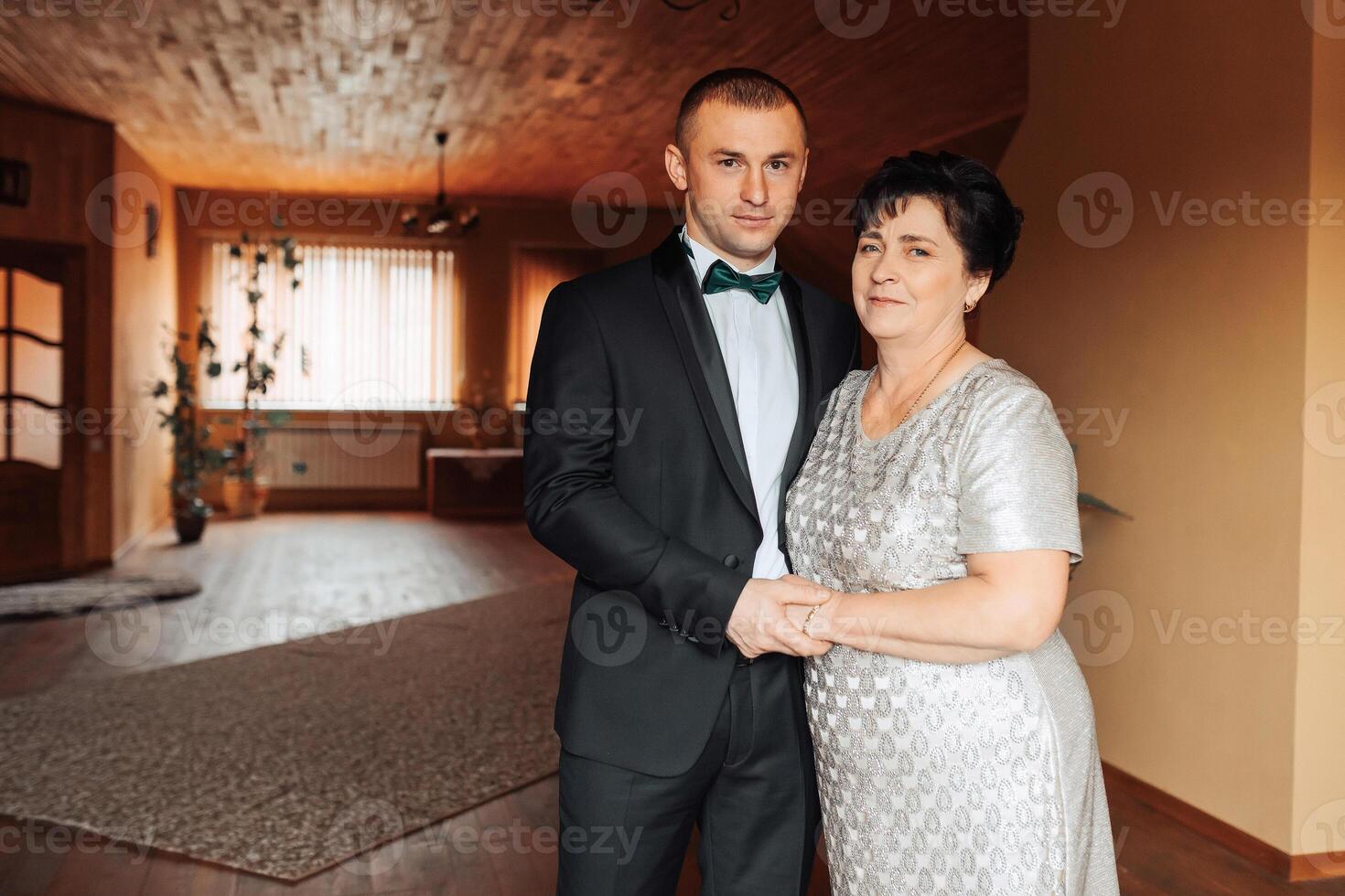 A man and a woman are standing in a room, the man wearing a suit photo