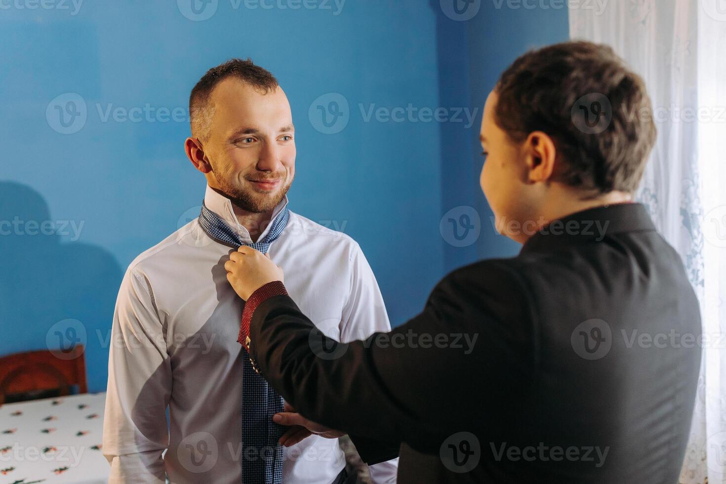A man is getting his tie tied by another man photo