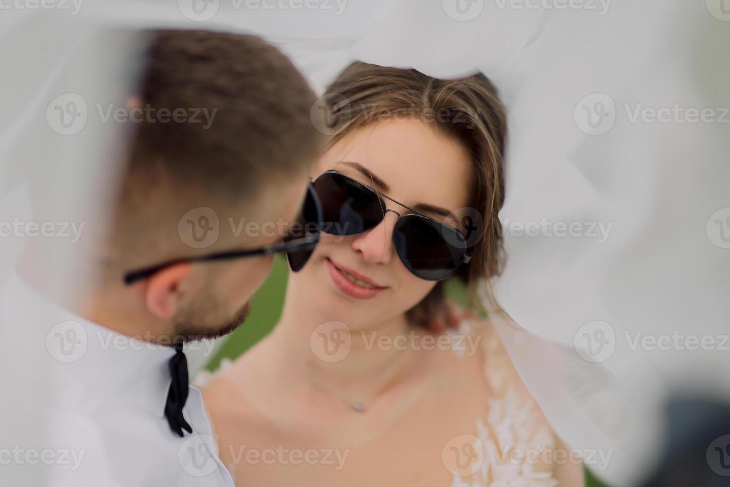 A bride and groom are posing for a picture with sunglasses on photo