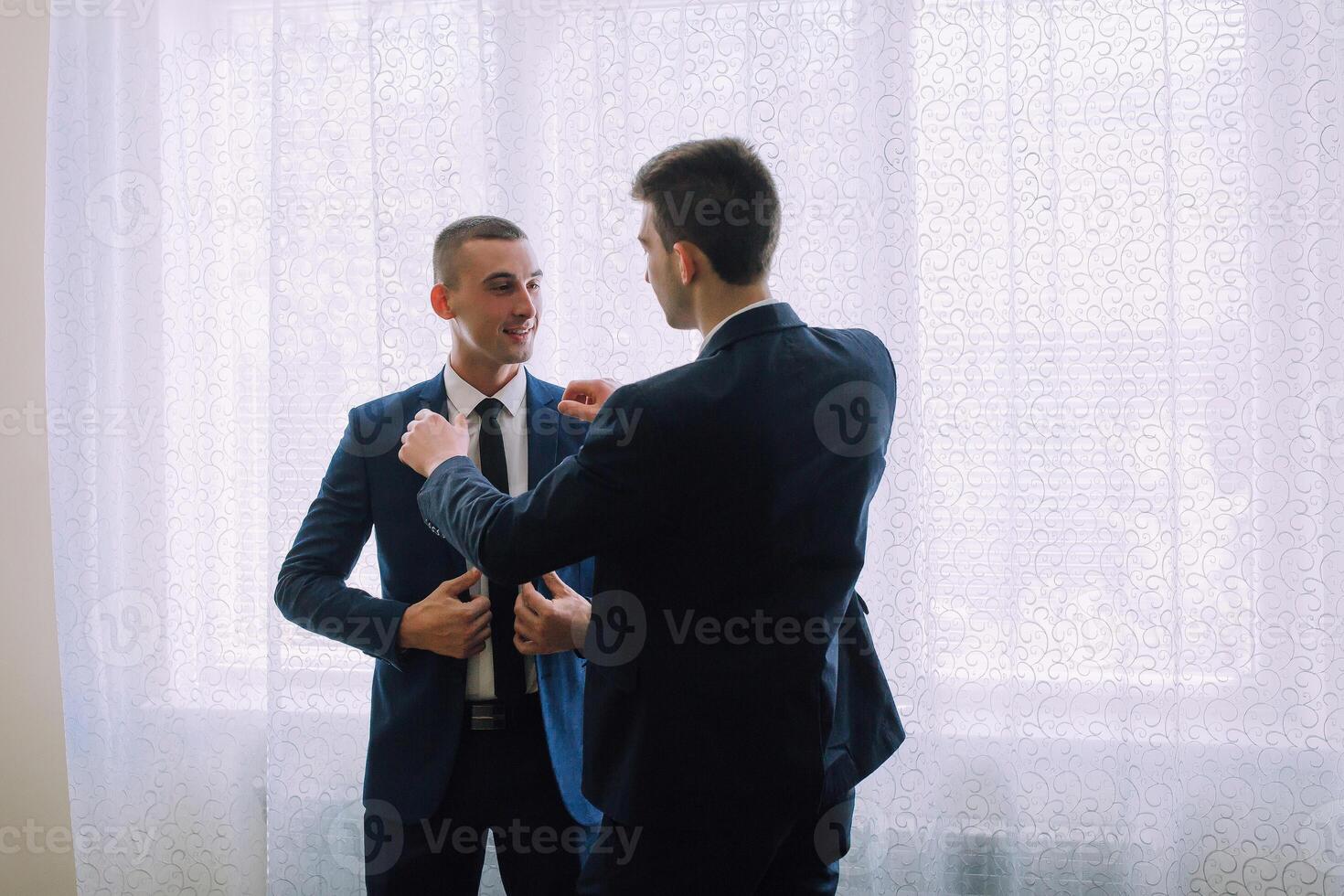 Two men in suits are standing in front of a window photo