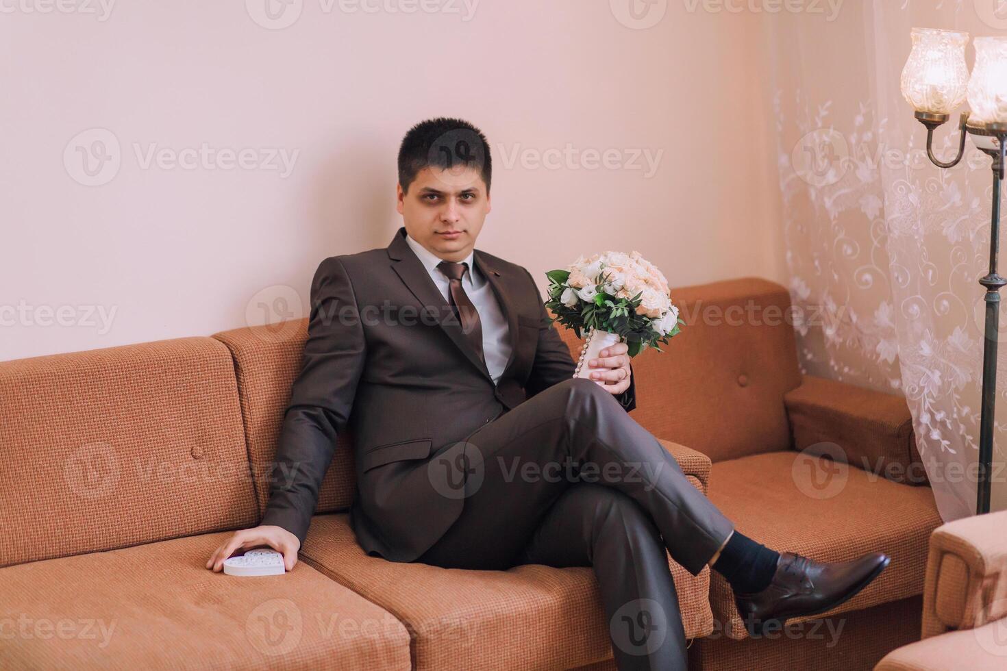 A man in a suit is sitting on a couch holding a bouquet of flowers photo