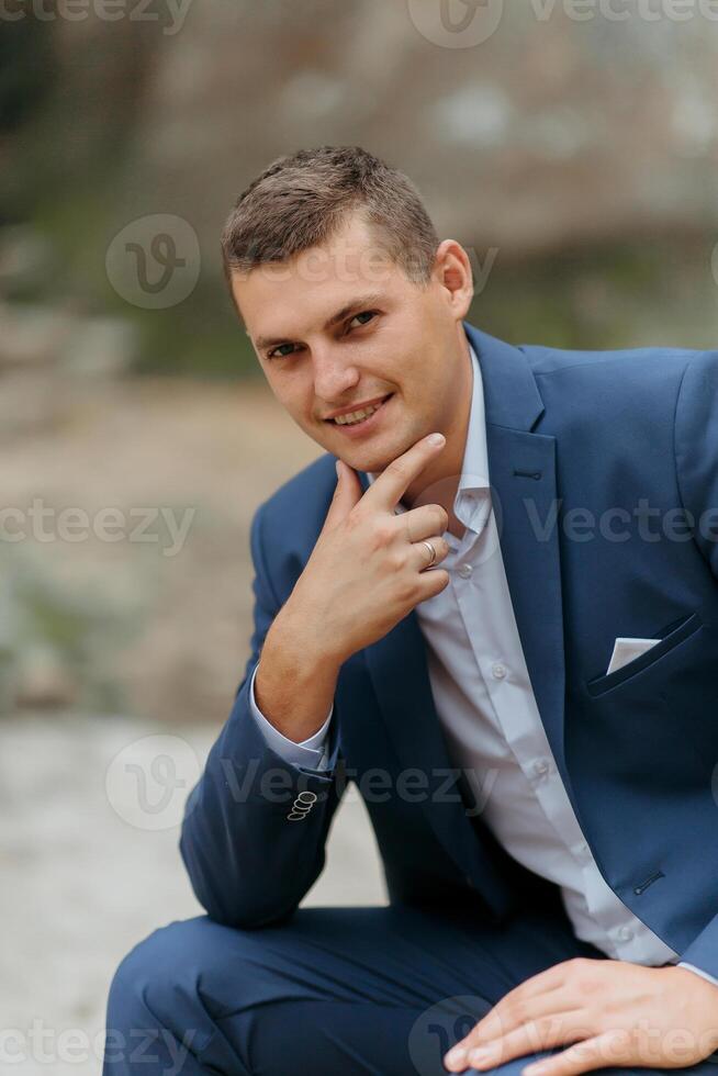 A man in a blue suit is sitting on the ground and looking at the camera photo