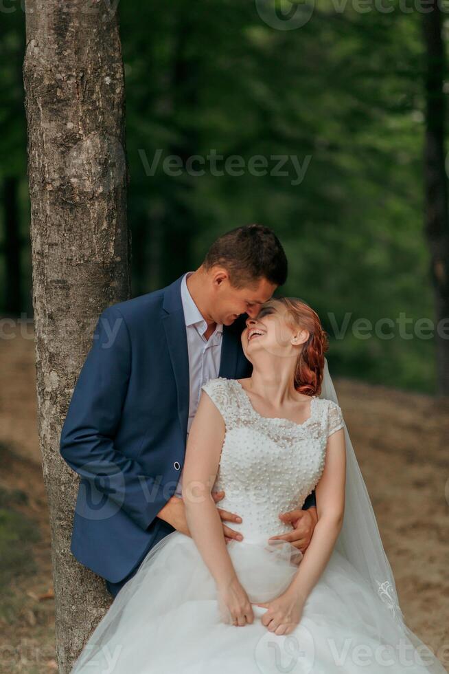 A bride and groom are sitting under a tree, smiling and hugging each other photo