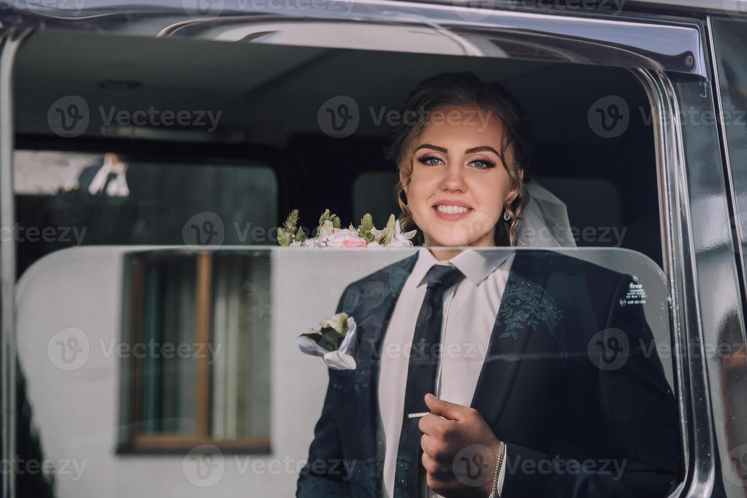 A man in a suit and tie is smiling as he stands in a car window photo