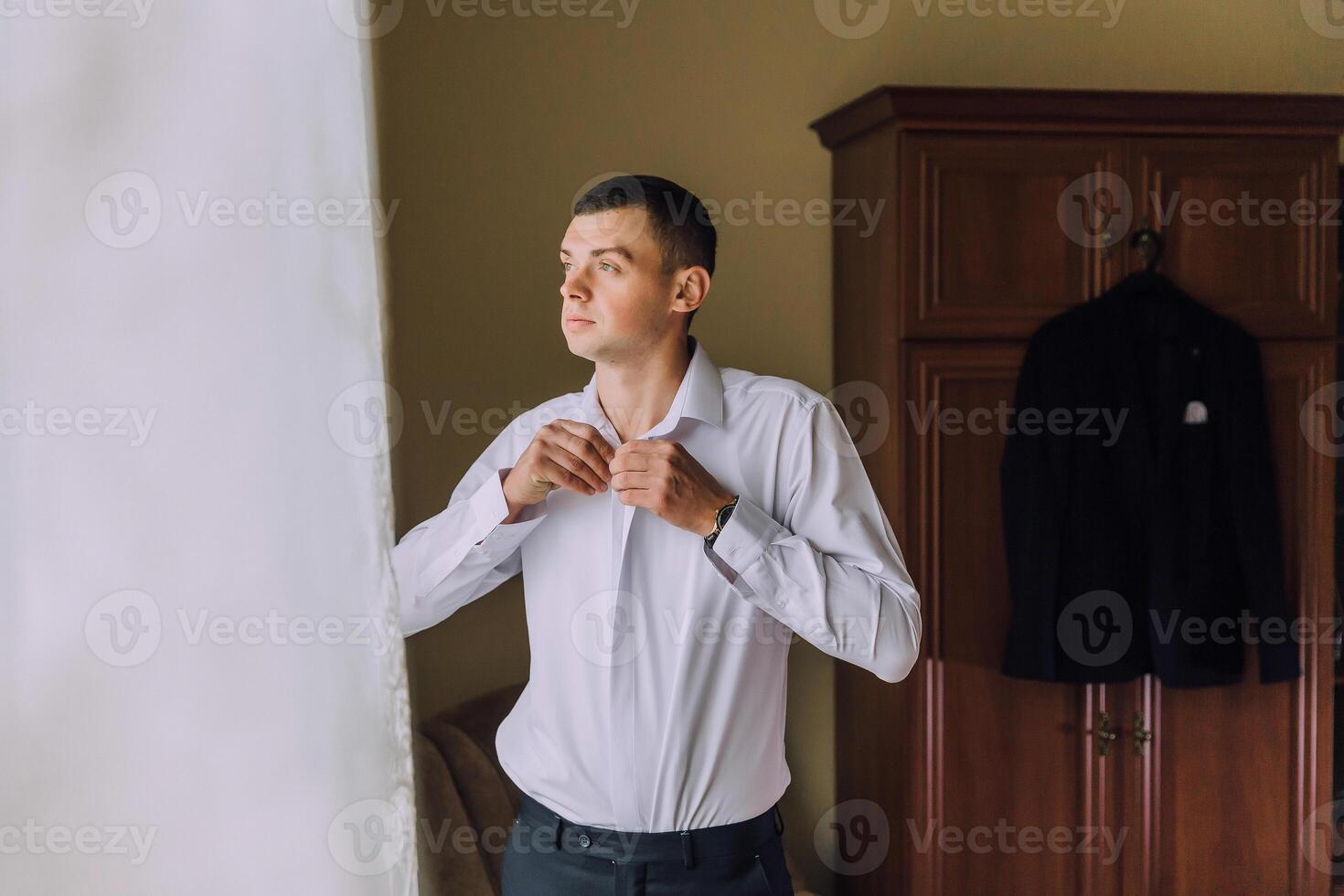 A man in a white shirt is getting dressed in front of a window photo