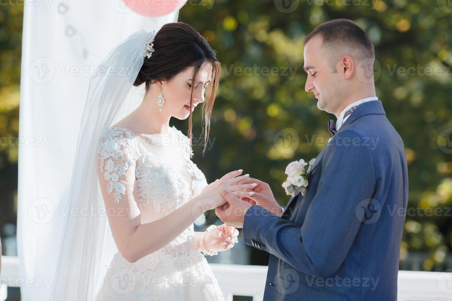 A bride and groom are getting married and the bride is wearing a white veil photo