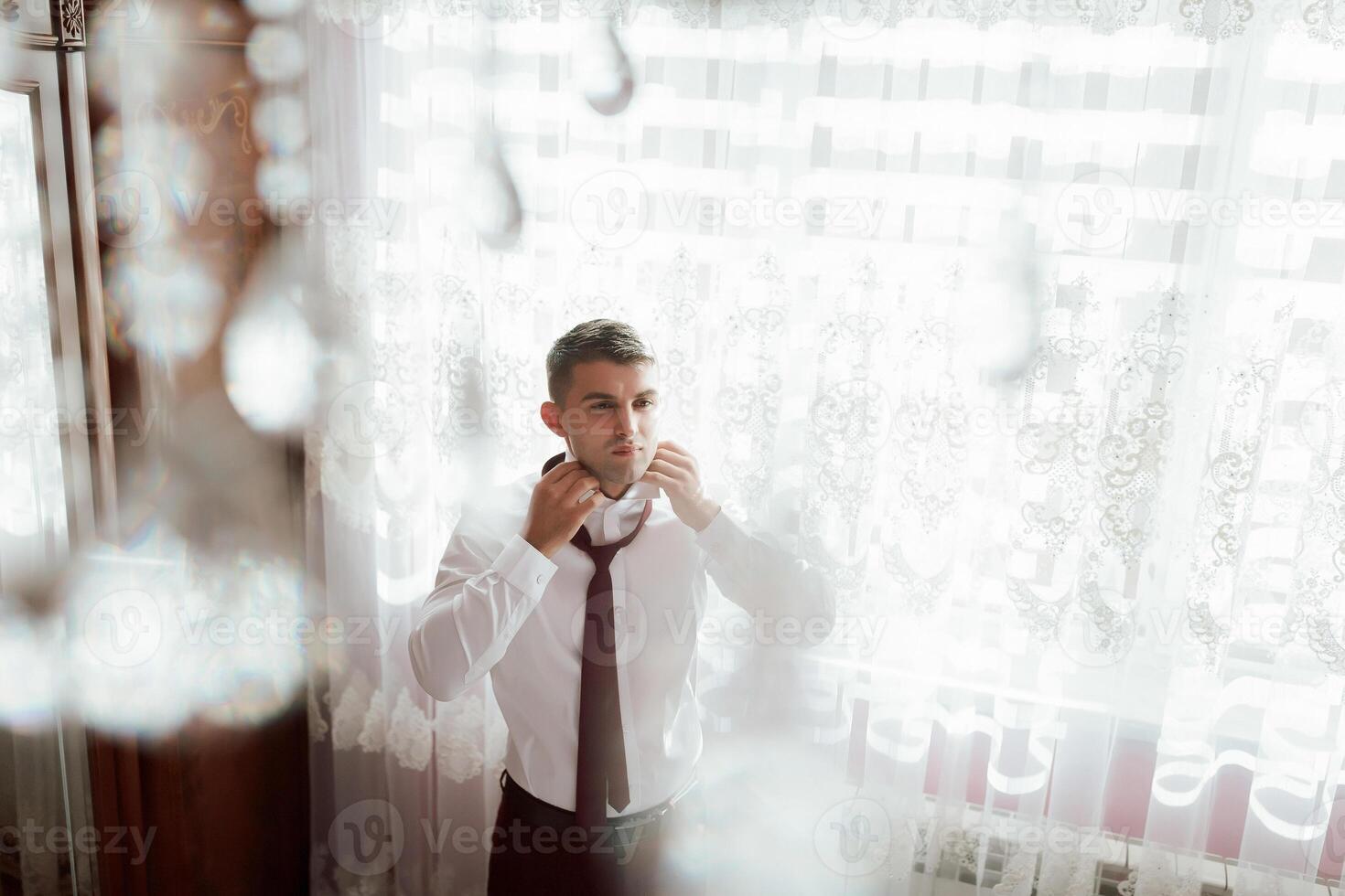 A man is getting ready for a wedding, putting on a tie and adjusting his collar photo