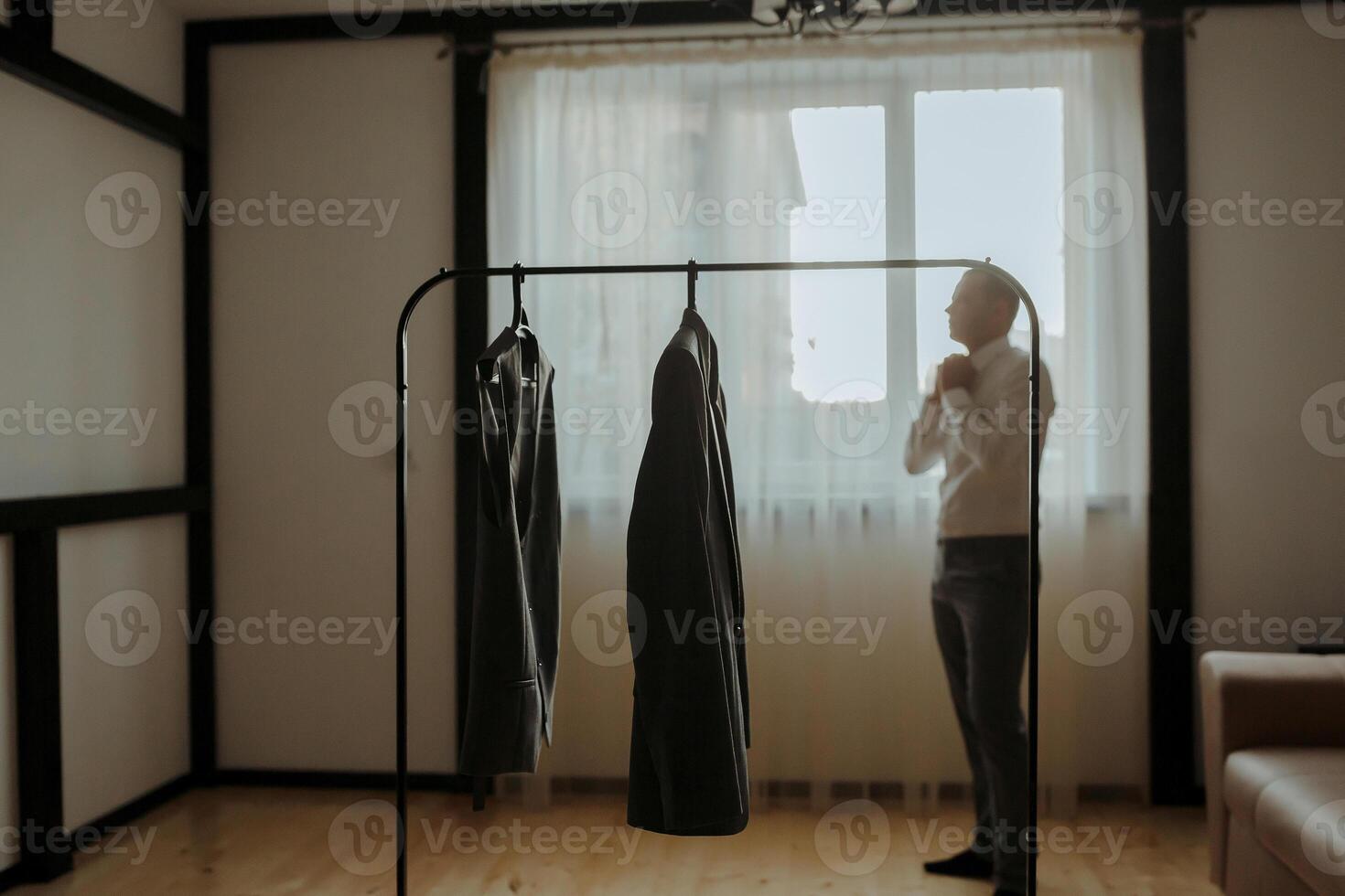 A man is standing in front of a clothes rack with a dress hanging from it photo