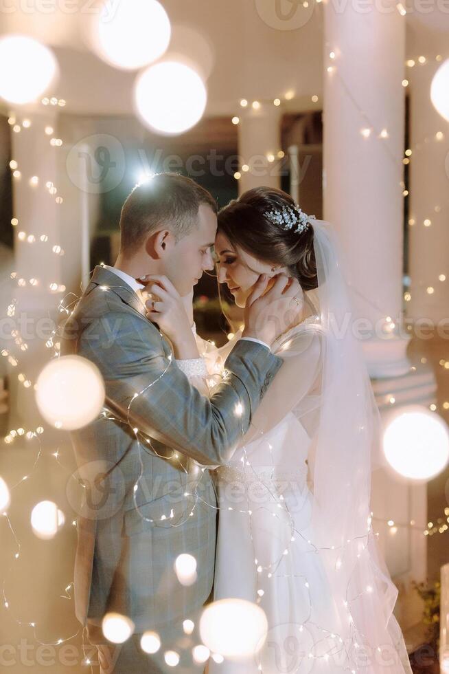 A bride and groom are embracing in front of a lighted backdrop photo