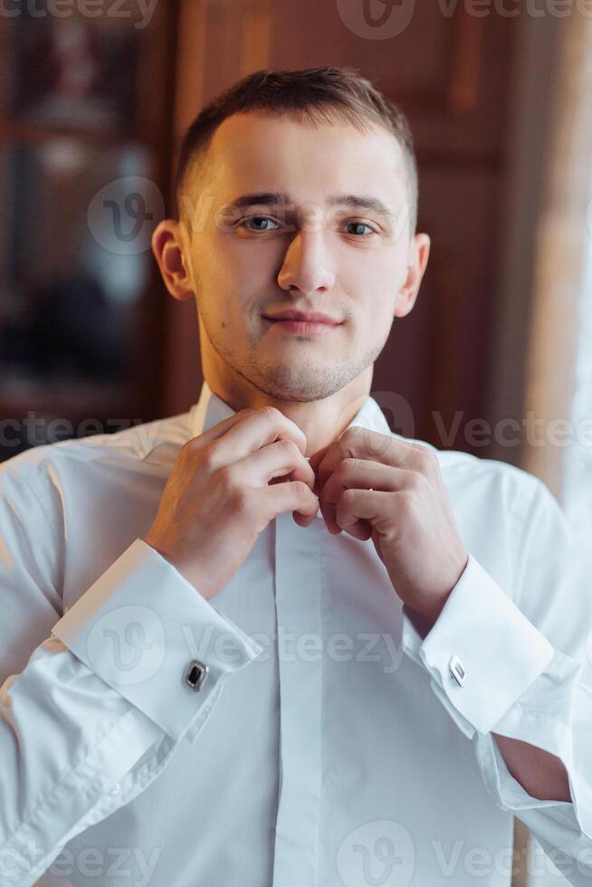 A man in a white shirt is getting dressed and adjusting his collar photo