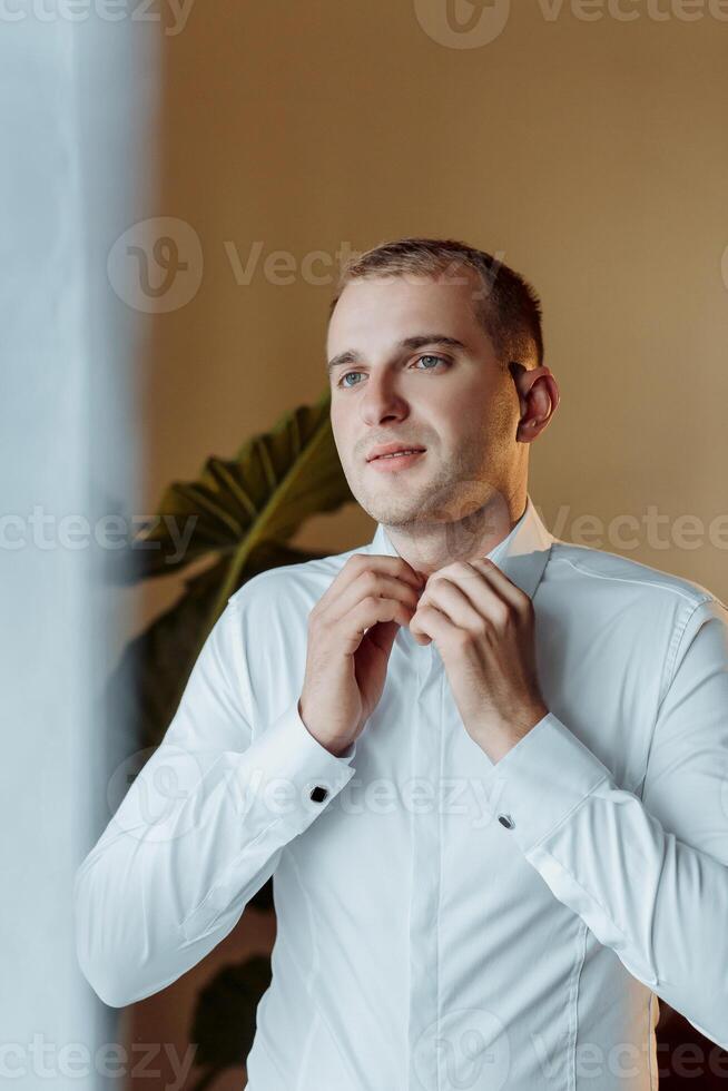 A man in a white shirt is getting dressed and adjusting his collar photo