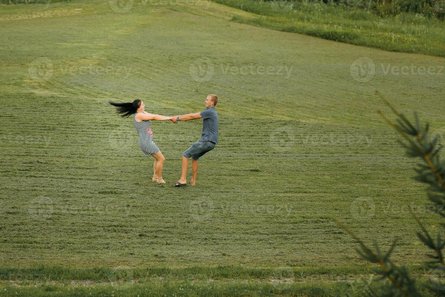 A couple is playing in a field, with the man holding the woman's hand photo