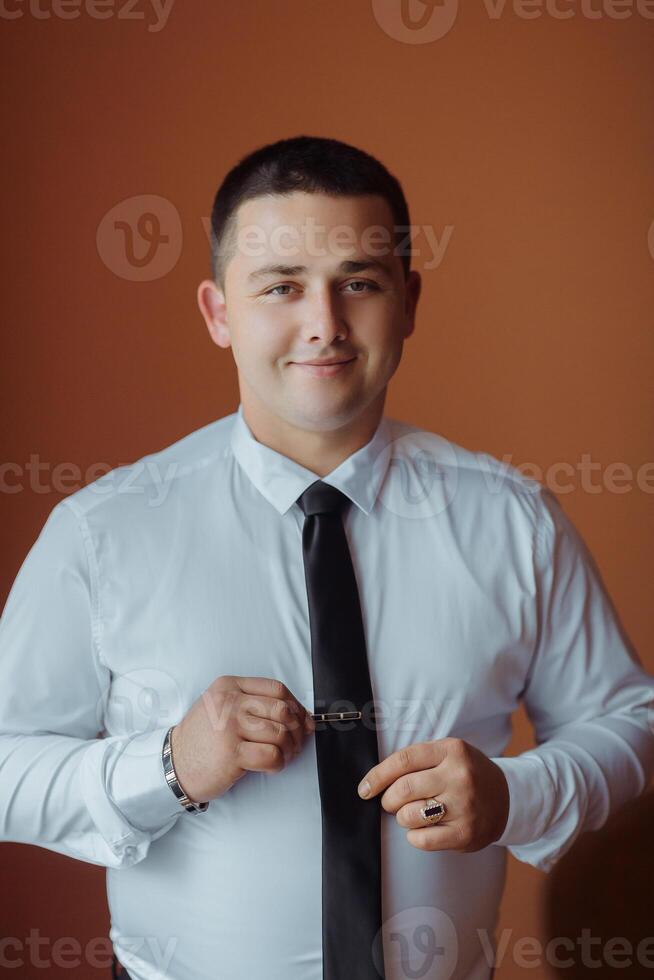 A man in a white shirt and black tie is smiling and adjusting his tie photo