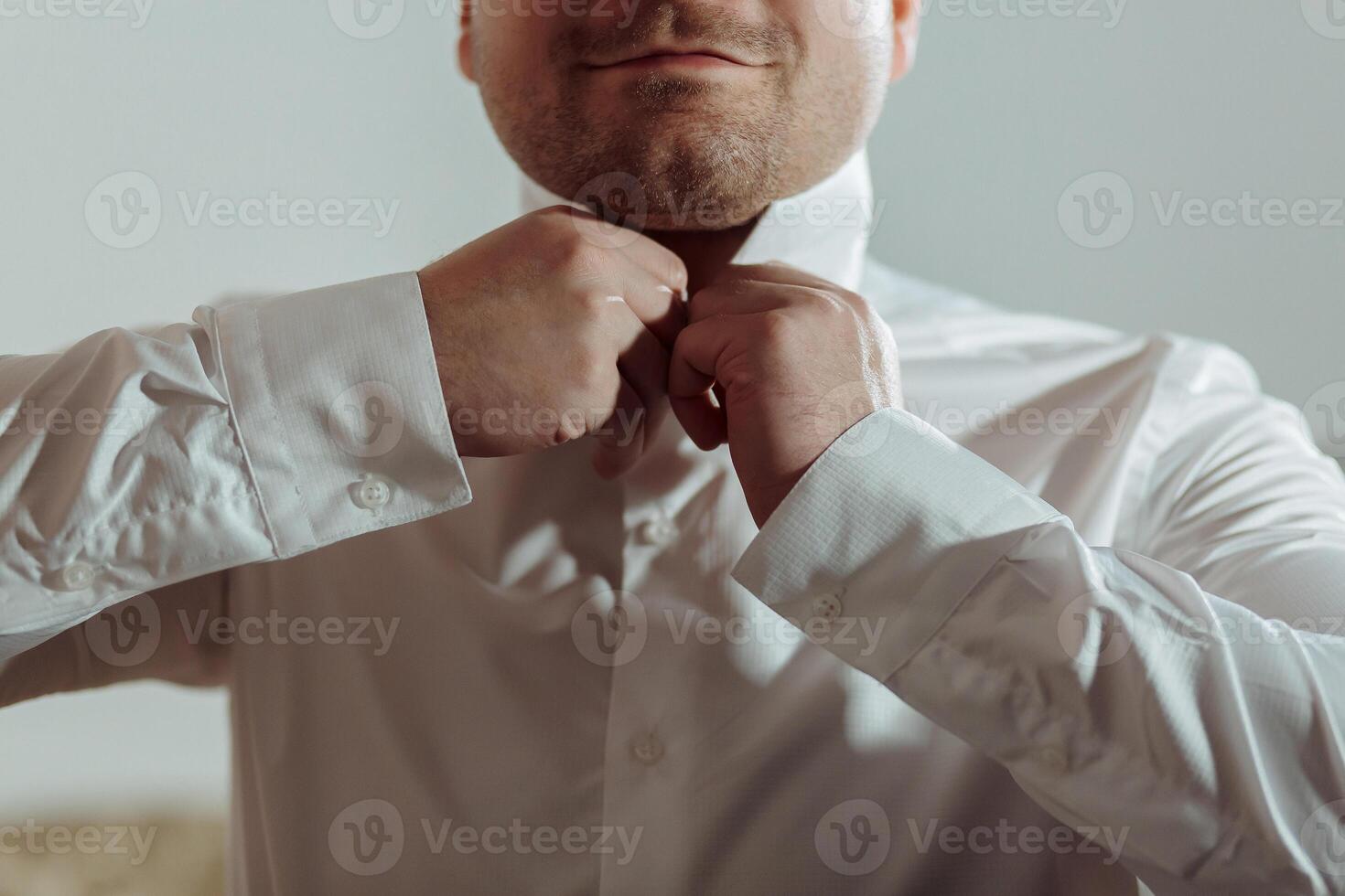 A man is getting dressed in a white shirt and is adjusting his collar photo