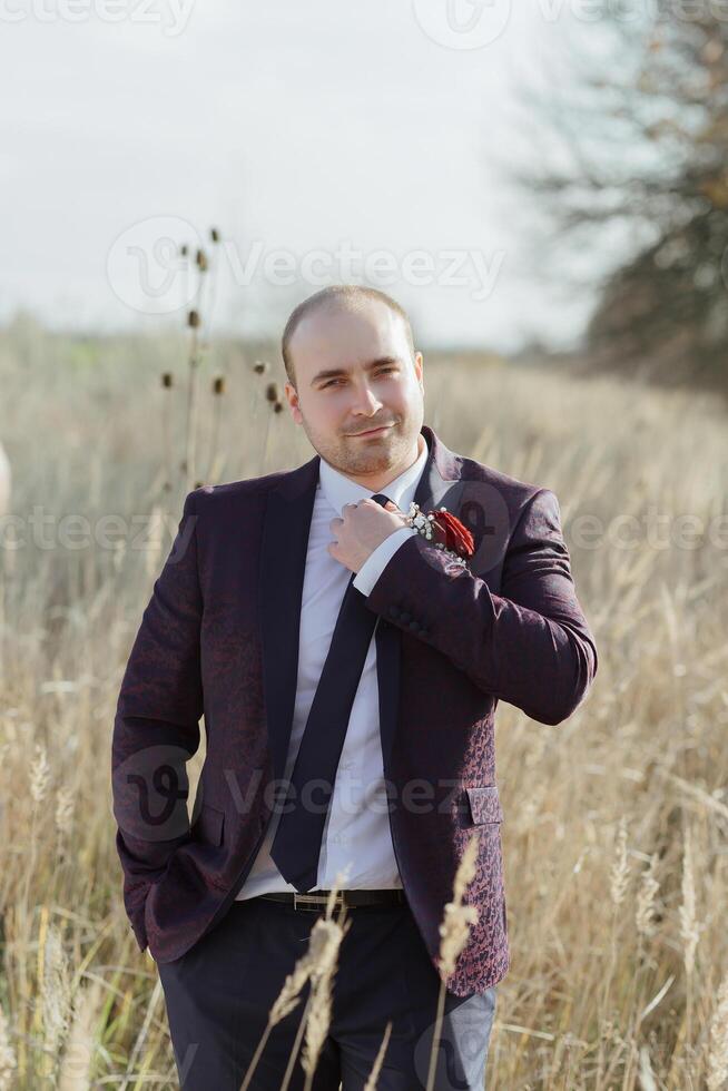 A man in a purple suit and tie stands in a field of tall grass photo