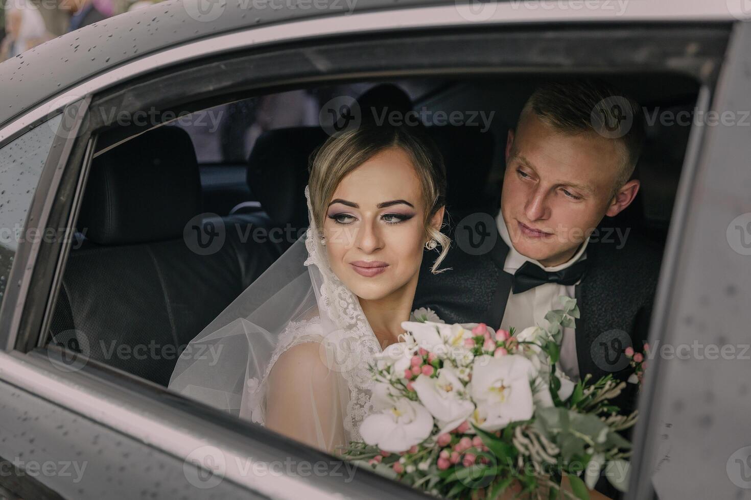 A bride and groom are in a car, with the bride holding a bouquet of flowers photo