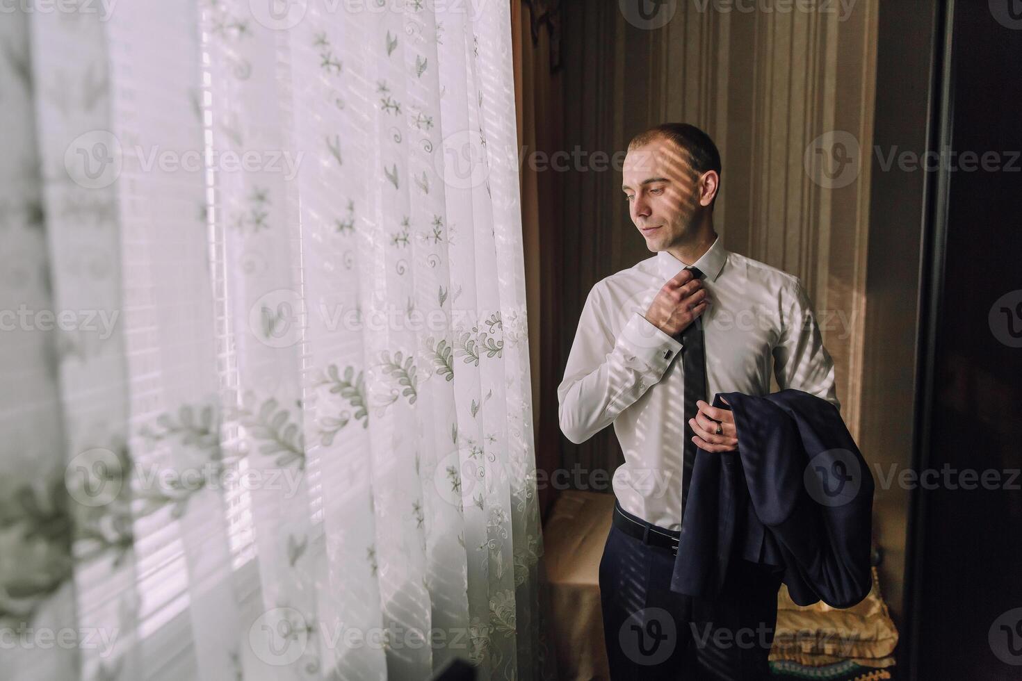A man is getting ready for a formal event, putting on a tie and jacket photo