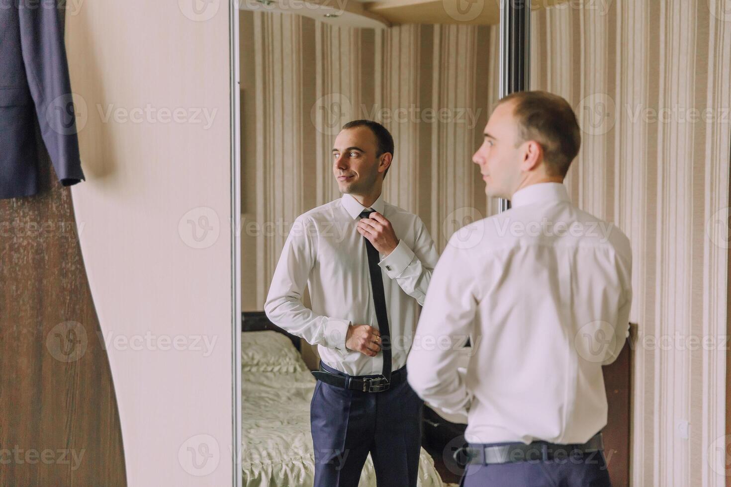 A man is getting ready for work and is adjusting his tie in front of a mirror photo
