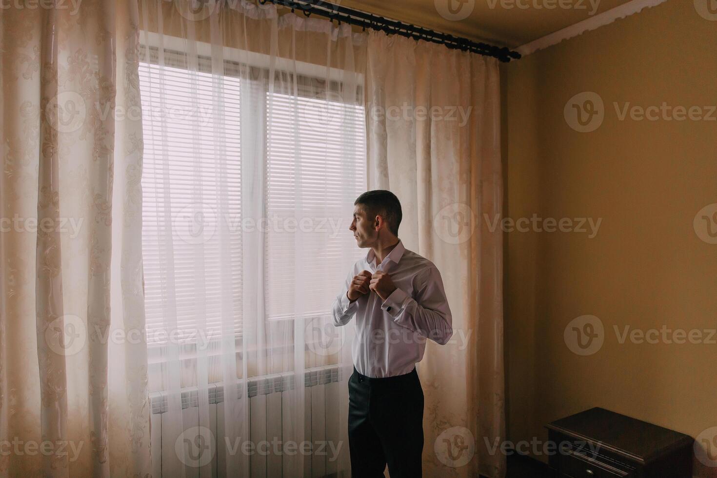 A man is getting dressed in front of a window photo