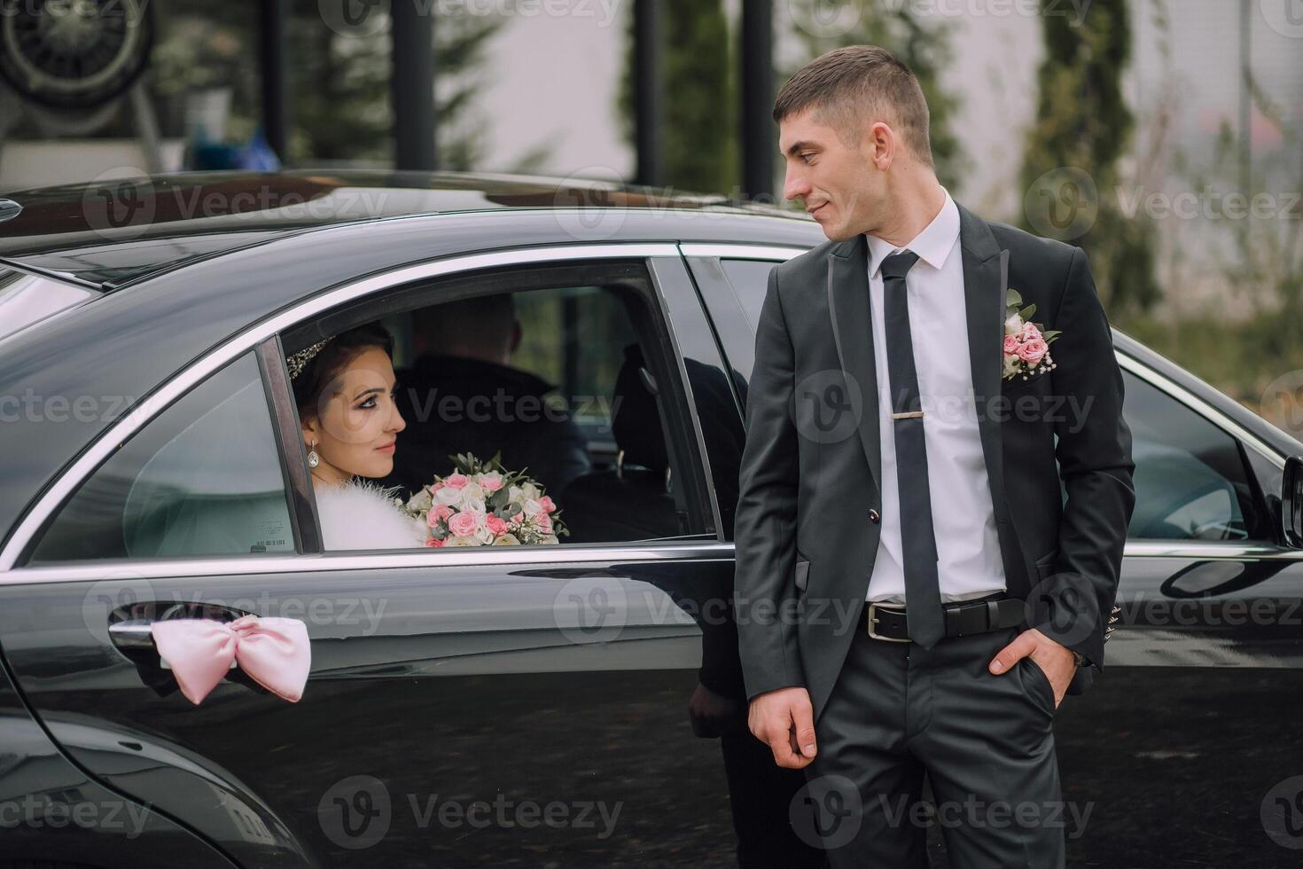 A man and a woman are standing in front of a black car photo