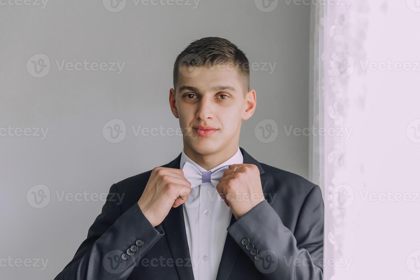 A man in a suit and tie is getting ready to tie his bow tie photo