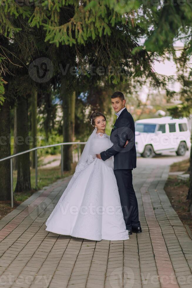 A bride and groom are posing for a picture in front of a white car photo