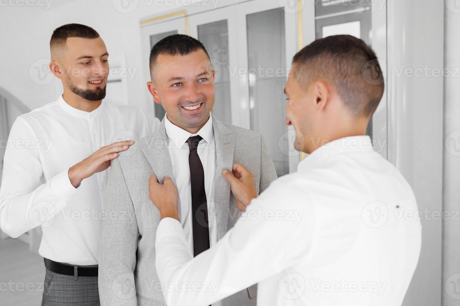 Three men are standing in a room, one of them is wearing a suit and tie photo