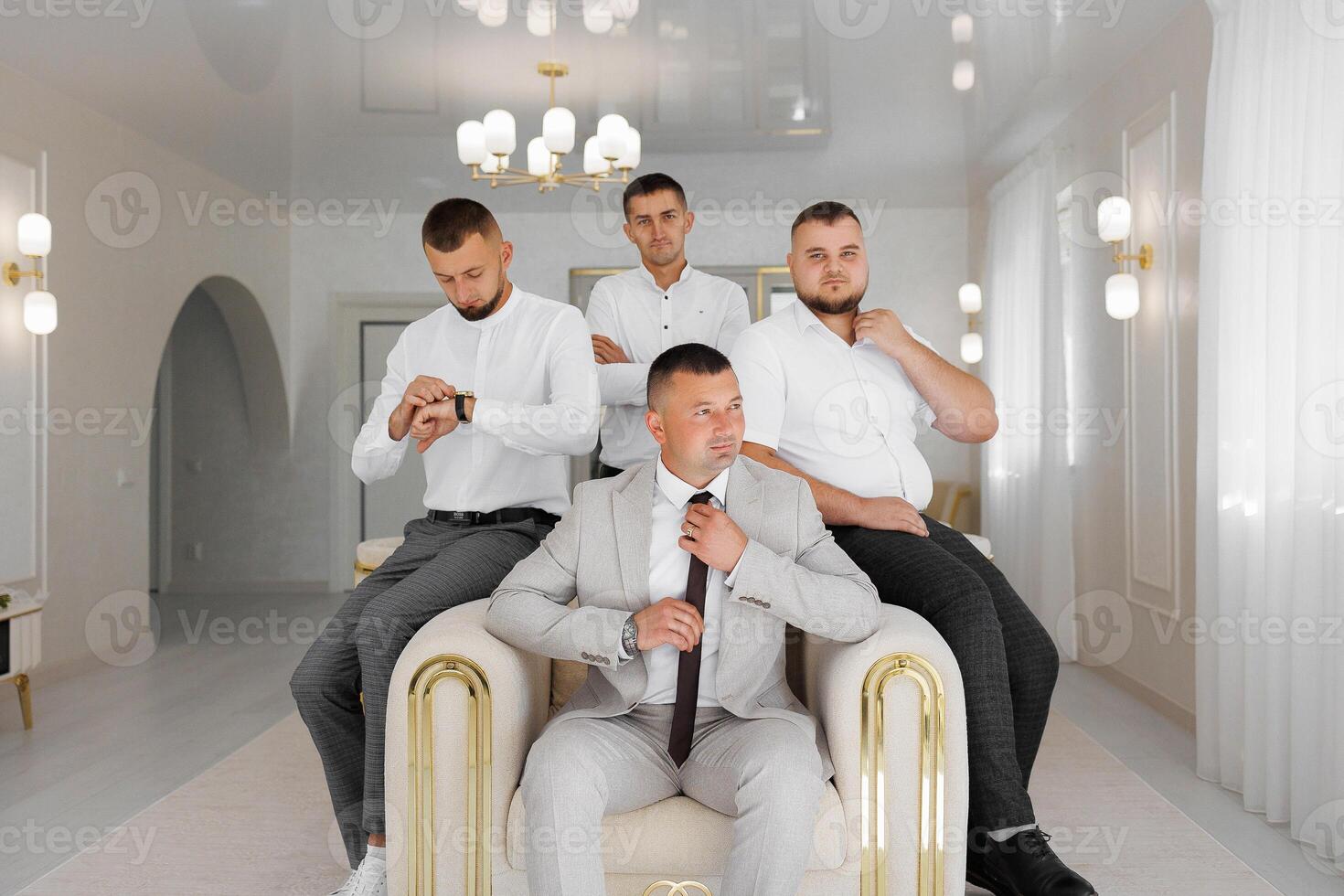 A man in a suit is sitting on a chair with three other men photo