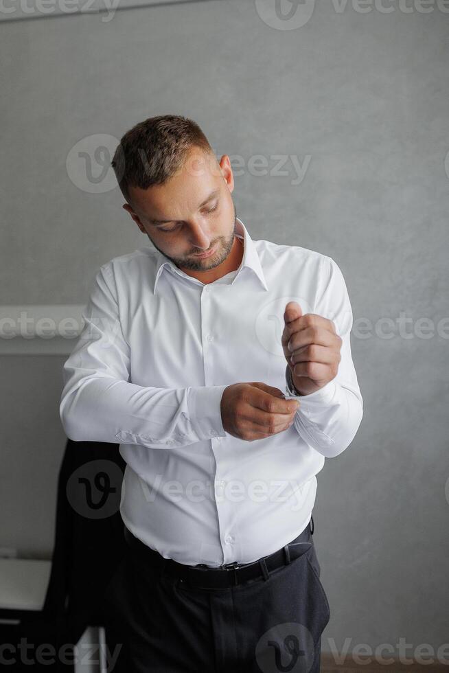 A man in a white shirt is getting dressed and adjusting his shirt photo