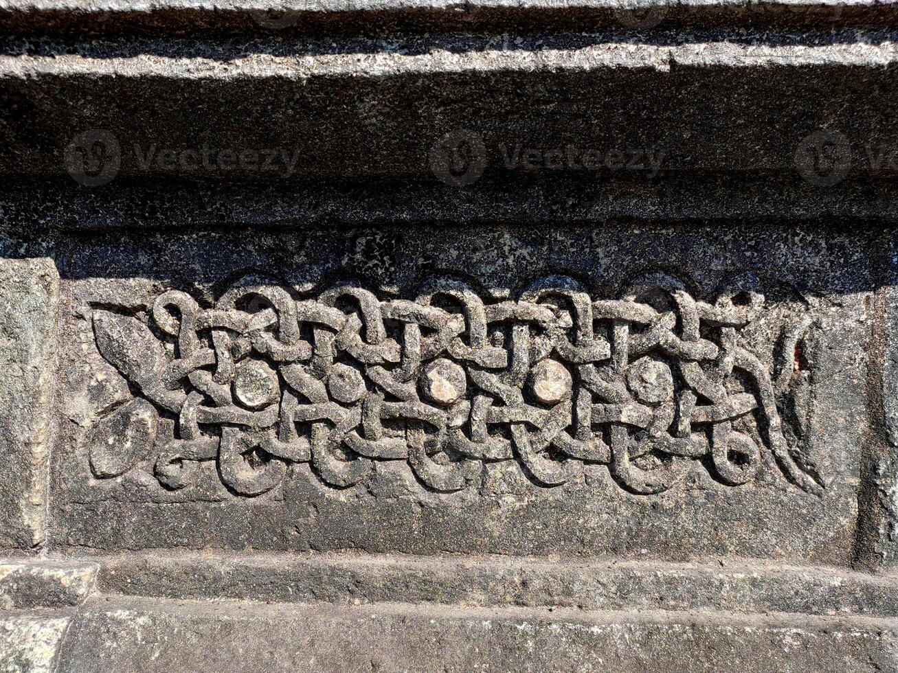 A detailed closeup of a snake carving on Halebidu Temples wall in Karnataka showcases Hoysala artistry, with precise scales, coiled form, and intricate light and shadow details. photo