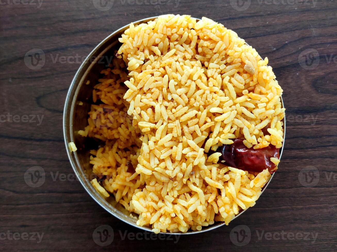 Closeup of onion rice in a stainless steel tiffin, vibrant yellow with red chili bits. The fluffy, well-cooked grains highlight this flavorful, spicy Indian dish. photo