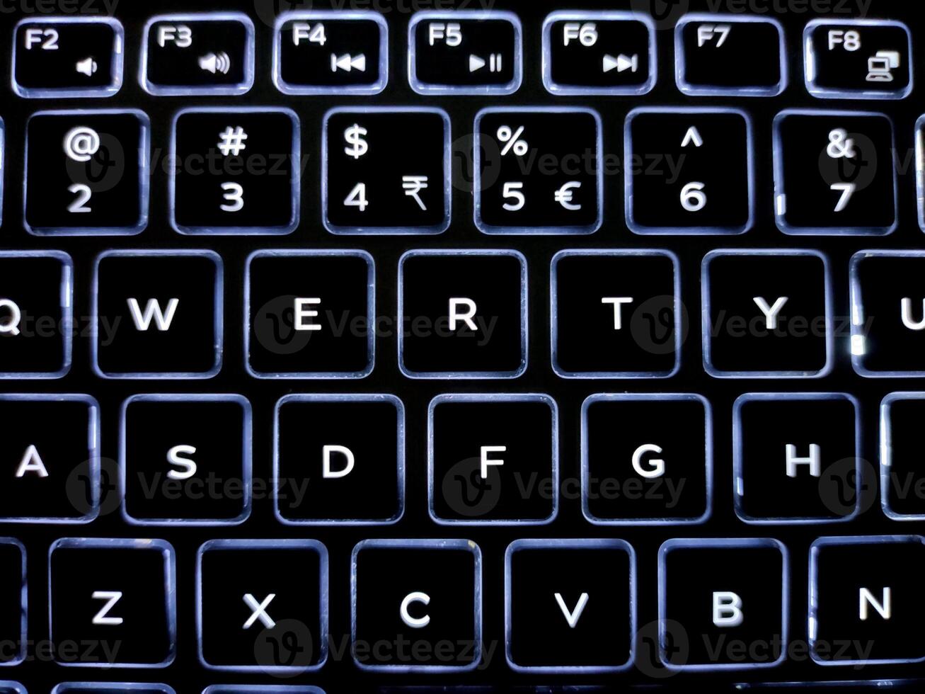 A close-up of a backlit keyboard with illuminated keys in a QWERTY layout. White letters on black keys contrast sharply, showcasing a sleek, modern design with a smooth, polished finish. photo