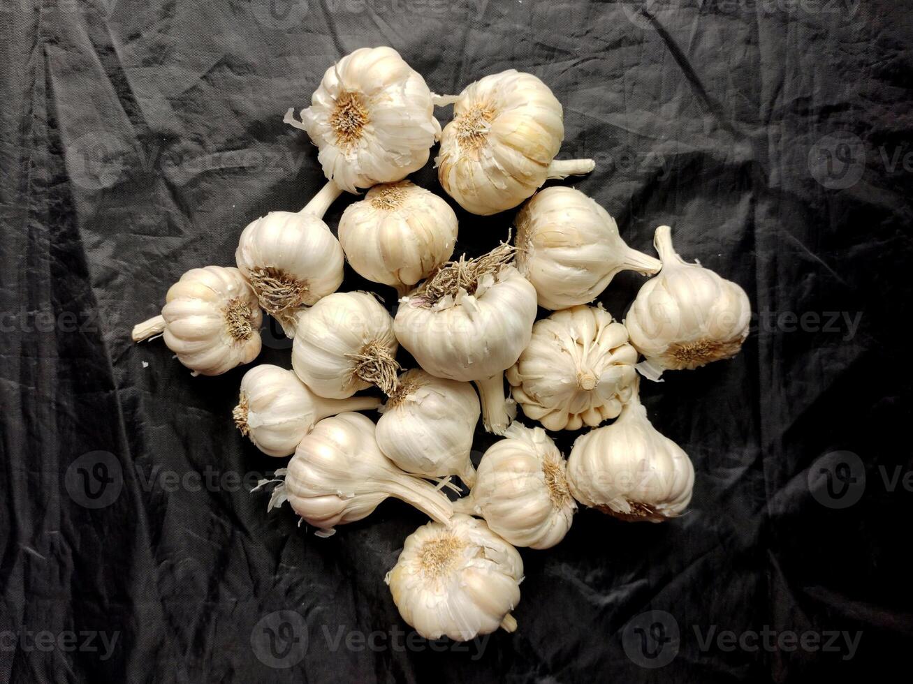A cluster of fresh garlic bulbs against a dark background, showcasing their papery skin, bulbous heads, and clove-packed structure, emphasizing their natural texture and unique shape. photo
