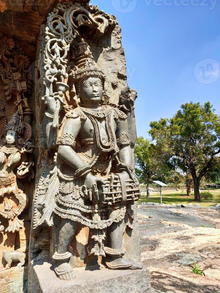 A close-up of a stone sculpture at Hoysaleswara Temple, Halebidu, Karnataka, depicting a musician with a drum. The intricate carving highlights Hoysala artisans' craftsmanship and attention to detail. photo
