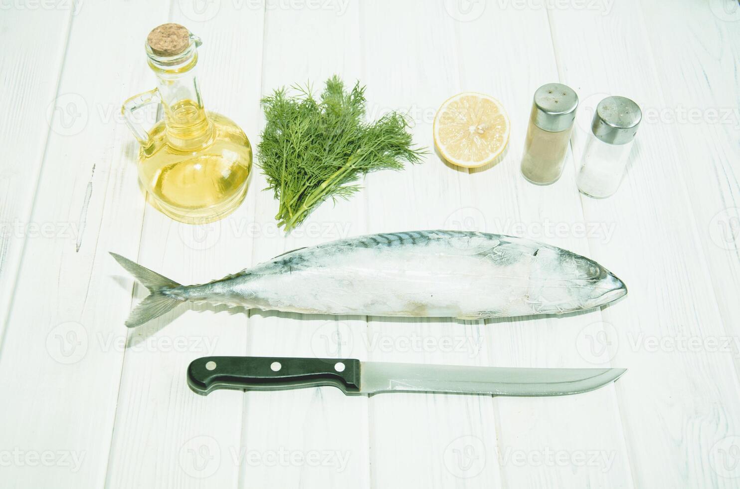 Fish, lemon, salt, pepper, and a knife on a white wooden table photo