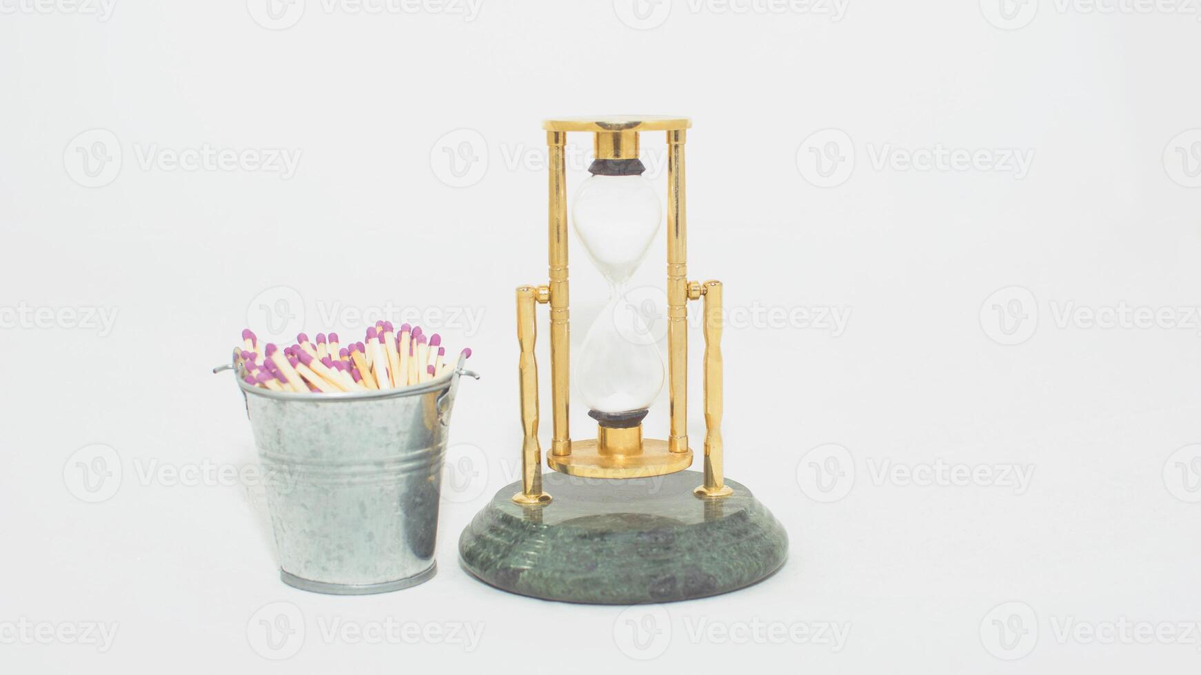 A gold and brass hourglass next to a bucket of matches photo