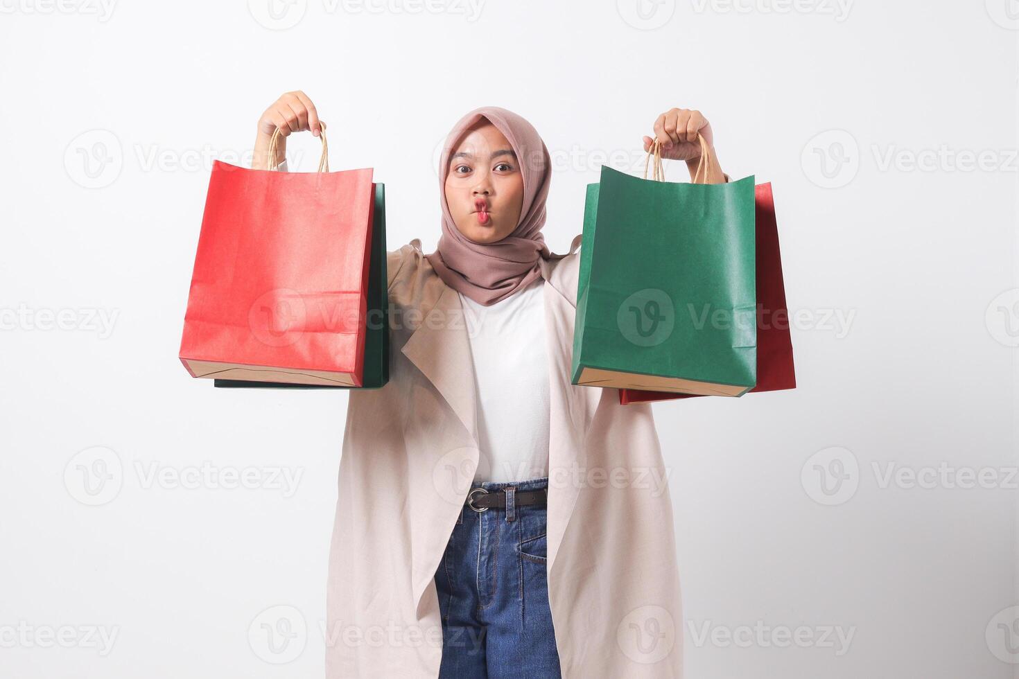 Portrait of attractive Asian hijab woman in casual suit holding and showing colorful paper shopping bags. Shopaholic girl and discount buying concept. Isolated image on white background photo