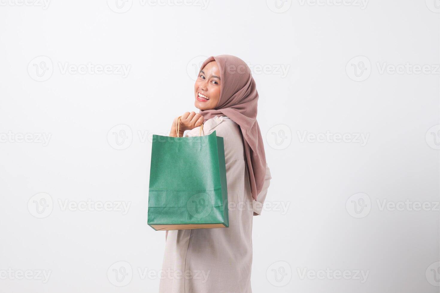 Portrait of cheerful Asian hijab woman in casual suit holding and showing colorful paper shopping bags. Shopaholic girl and discount buying concept. Isolated image on white background photo