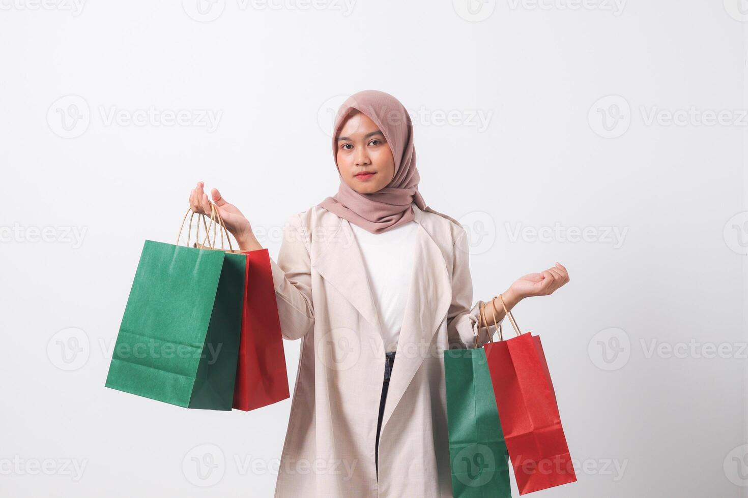 Portrait of attractive Asian hijab woman in casual suit holding and showing colorful paper shopping bags. Shopaholic girl and discount buying concept. Isolated image on white background photo