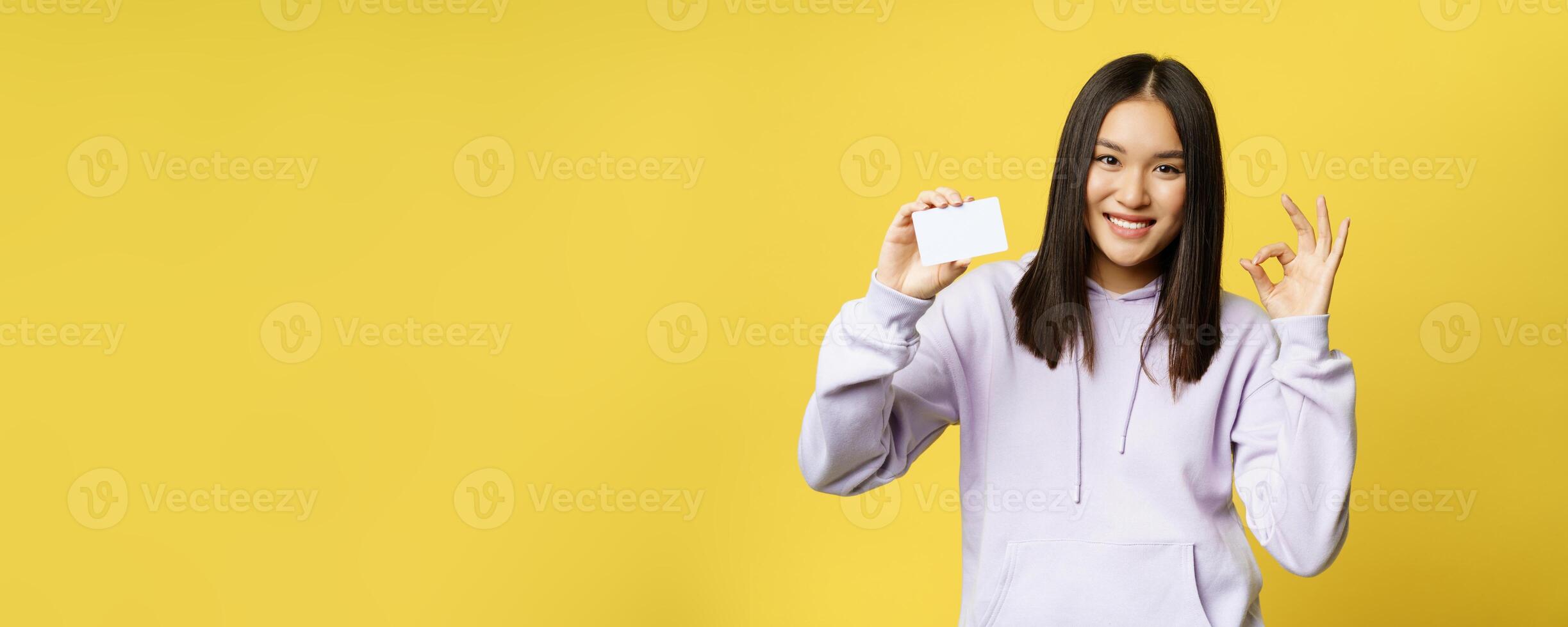 Image of korean girl shows credit card and okay sign, shopping concept, recommending store, yellow background photo